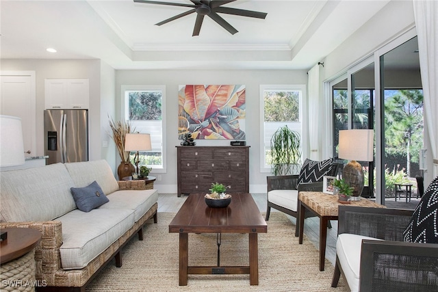 living area featuring a raised ceiling, a wealth of natural light, light hardwood / wood-style flooring, and ceiling fan