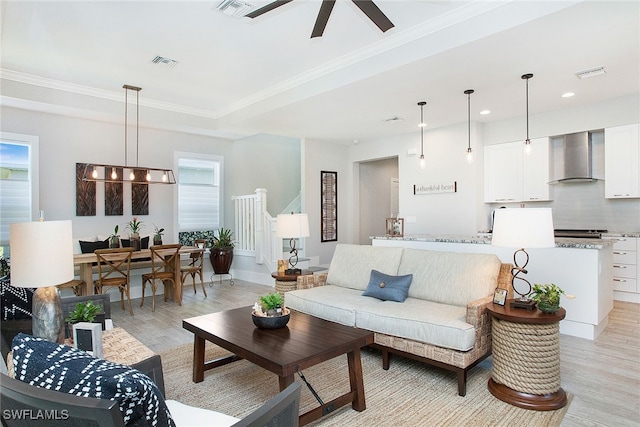 living room with light wood-type flooring, a tray ceiling, ceiling fan, and ornamental molding