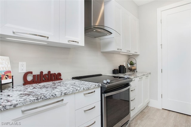 kitchen with stainless steel range with electric stovetop, wall chimney exhaust hood, light hardwood / wood-style floors, and white cabinets