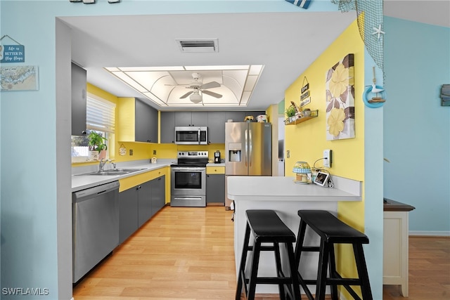 kitchen featuring gray cabinetry, ceiling fan, sink, stainless steel appliances, and a kitchen breakfast bar