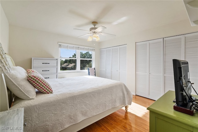 bedroom with two closets, light hardwood / wood-style flooring, and ceiling fan