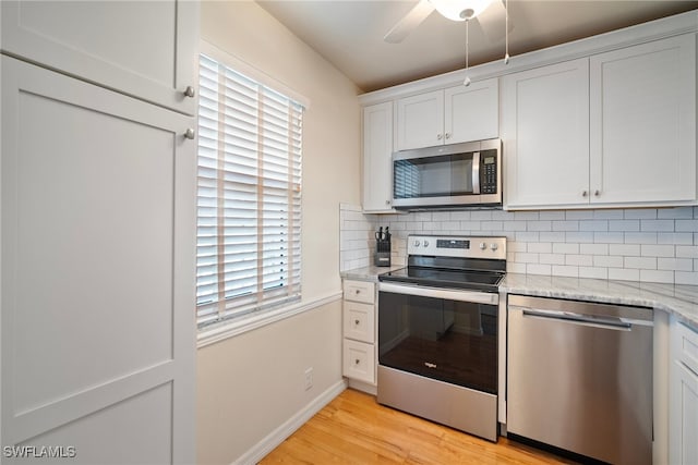 kitchen with decorative backsplash, appliances with stainless steel finishes, light wood-type flooring, light stone countertops, and white cabinets