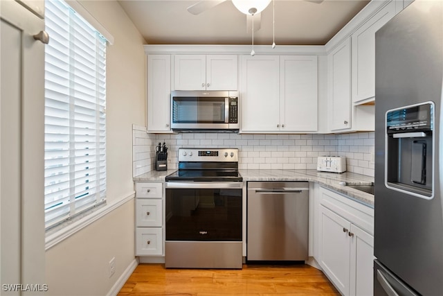 kitchen with light stone countertops, light wood-type flooring, stainless steel appliances, and white cabinetry