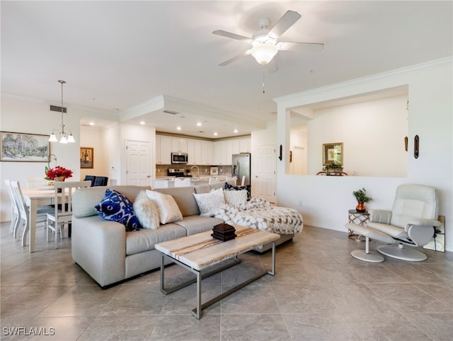 living room with ceiling fan with notable chandelier, sink, light tile patterned floors, and crown molding