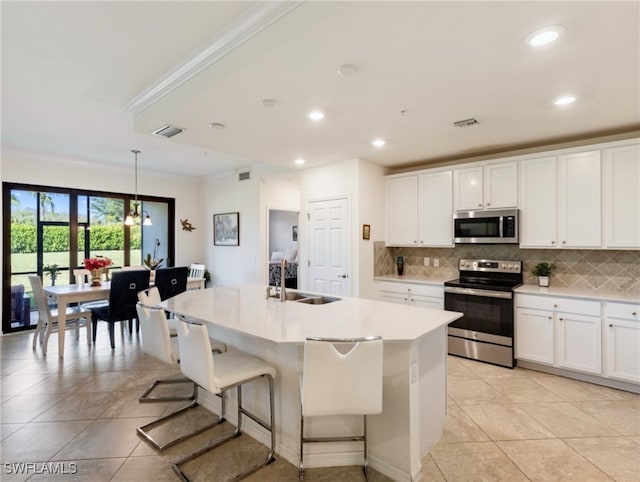 kitchen featuring appliances with stainless steel finishes, a center island with sink, white cabinetry, and decorative light fixtures