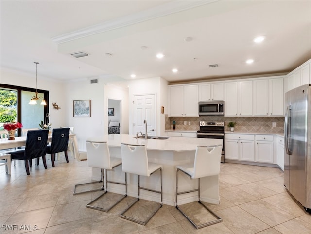 kitchen with white cabinetry, sink, hanging light fixtures, stainless steel appliances, and a kitchen island with sink