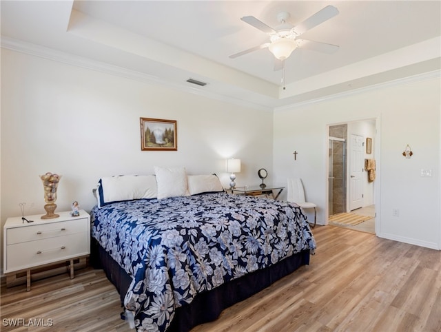 bedroom featuring light hardwood / wood-style flooring, ceiling fan, ornamental molding, connected bathroom, and a tray ceiling