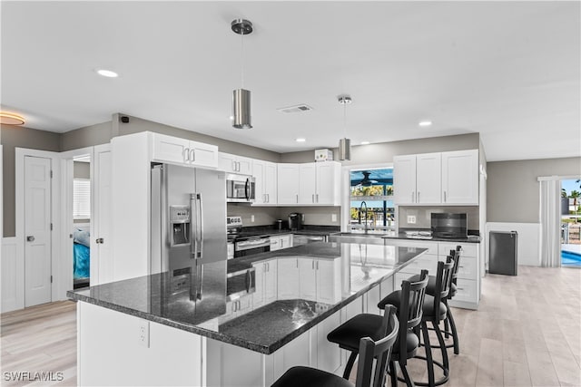 kitchen with white cabinets, light wood-type flooring, stainless steel appliances, and hanging light fixtures