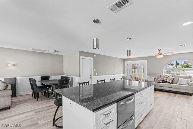 kitchen featuring white cabinets, hanging light fixtures, dark stone countertops, a kitchen island, and a kitchen bar