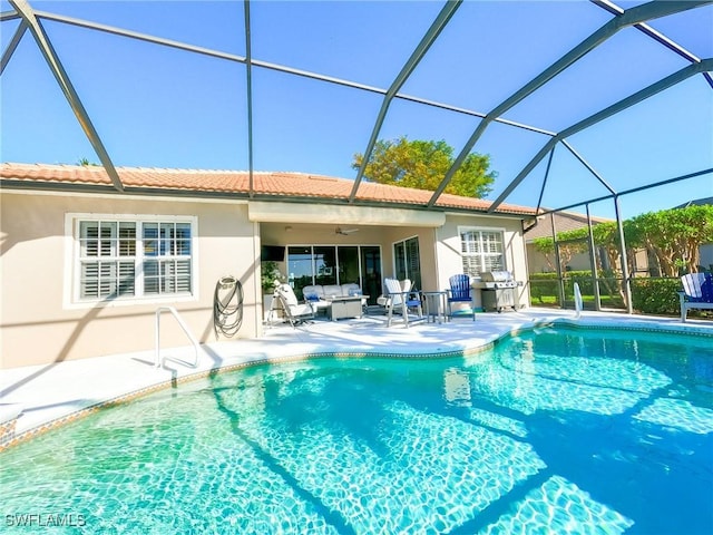 view of pool with outdoor lounge area, ceiling fan, glass enclosure, a grill, and a patio