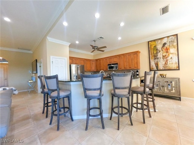 kitchen featuring ceiling fan, a kitchen breakfast bar, appliances with stainless steel finishes, light tile patterned floors, and ornamental molding