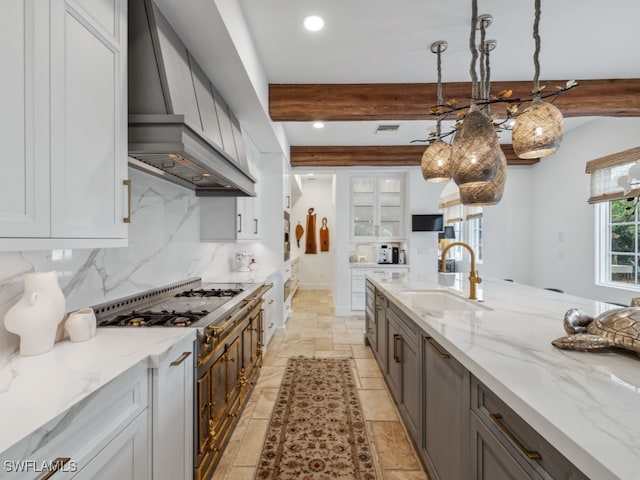 kitchen featuring premium range hood, light stone counters, sink, pendant lighting, and beamed ceiling