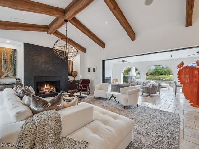 living room with a fireplace, vaulted ceiling with beams, and ceiling fan with notable chandelier