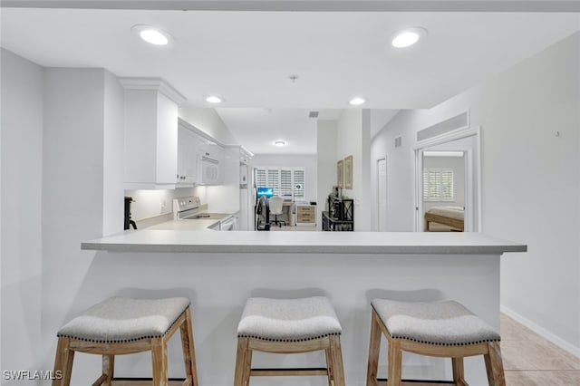 kitchen featuring kitchen peninsula, stainless steel range with electric stovetop, white cabinets, a breakfast bar area, and light tile patterned flooring