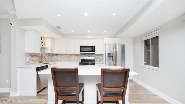 kitchen featuring sink, white cabinetry, stainless steel appliances, a center island, and decorative backsplash