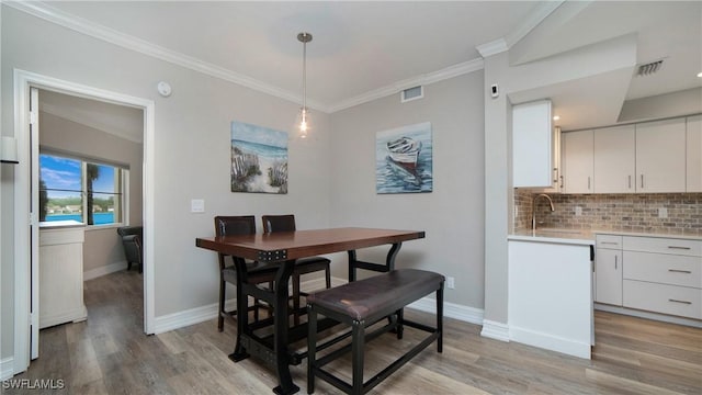 dining area with ornamental molding, sink, and light hardwood / wood-style floors