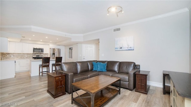 living room featuring sink, crown molding, and light wood-type flooring