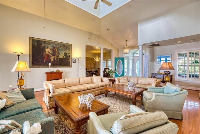 living room featuring decorative columns, high vaulted ceiling, ceiling fan with notable chandelier, and hardwood / wood-style flooring