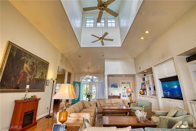 living room featuring decorative columns, ceiling fan, wood-type flooring, and a high ceiling