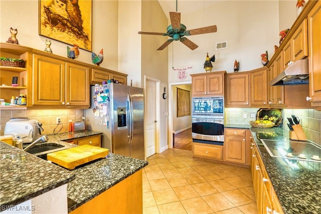 kitchen featuring ceiling fan, stainless steel appliances, a high ceiling, tasteful backsplash, and light tile patterned floors