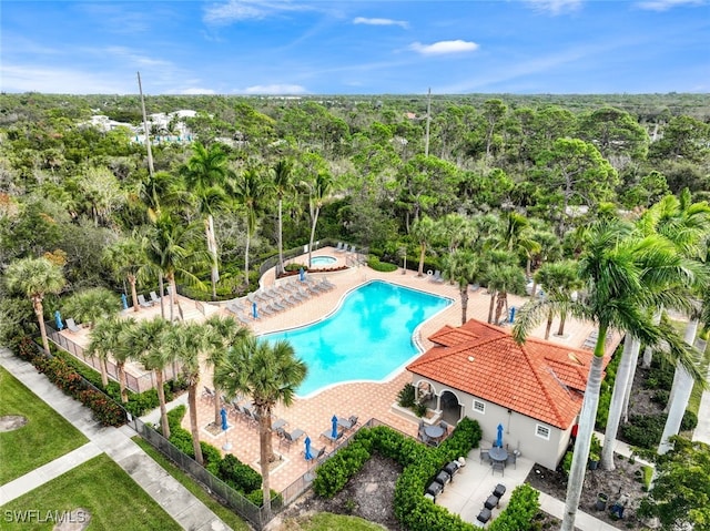 community pool featuring fence, a community hot tub, a view of trees, and a patio