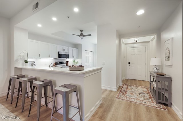 kitchen with a breakfast bar area, stainless steel appliances, visible vents, light wood-style floors, and a peninsula