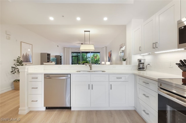 kitchen featuring white cabinets, light wood-style flooring, a peninsula, stainless steel appliances, and a sink