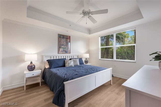 bedroom with a raised ceiling, crown molding, and light wood-style flooring