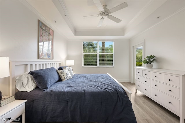 bedroom with ornamental molding, ceiling fan, light wood finished floors, and a raised ceiling