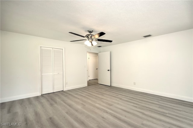 unfurnished bedroom with ceiling fan, a closet, a textured ceiling, and light wood-type flooring