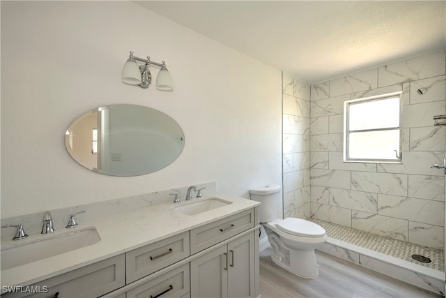 bathroom featuring hardwood / wood-style flooring, vanity, toilet, and a tile shower