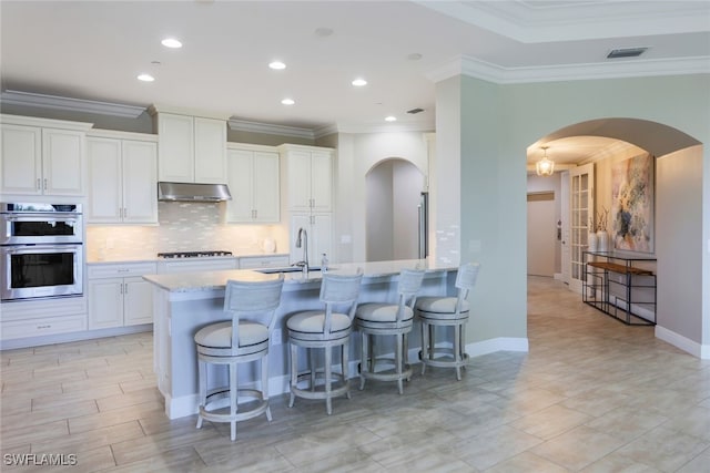 kitchen with light stone countertops, stainless steel double oven, gas stovetop, crown molding, and white cabinetry