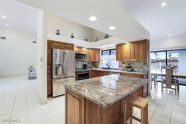 kitchen featuring a center island, light tile patterned floors, light stone countertops, appliances with stainless steel finishes, and tasteful backsplash