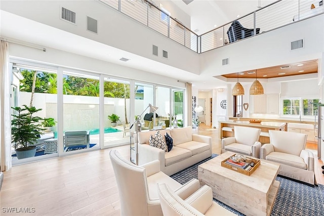 living room featuring a towering ceiling, a healthy amount of sunlight, and light wood-type flooring