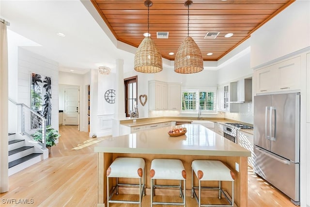 kitchen with appliances with stainless steel finishes, wall chimney exhaust hood, light hardwood / wood-style flooring, wooden ceiling, and white cabinetry