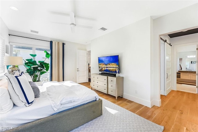 bedroom with a barn door, ensuite bathroom, light hardwood / wood-style flooring, and ceiling fan