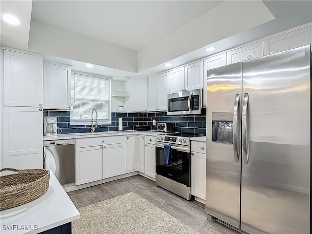 kitchen with appliances with stainless steel finishes, light wood-type flooring, tasteful backsplash, sink, and white cabinetry