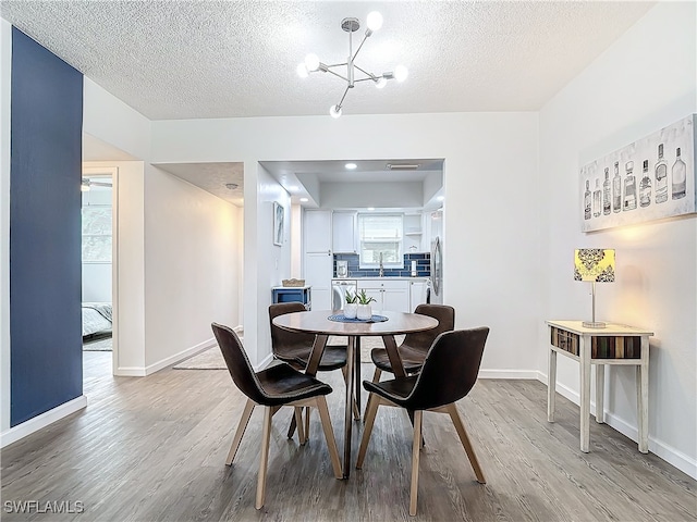 dining area featuring a textured ceiling, a notable chandelier, light wood-type flooring, and sink