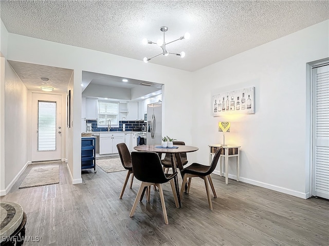 dining room featuring a notable chandelier, sink, a textured ceiling, and light wood-type flooring