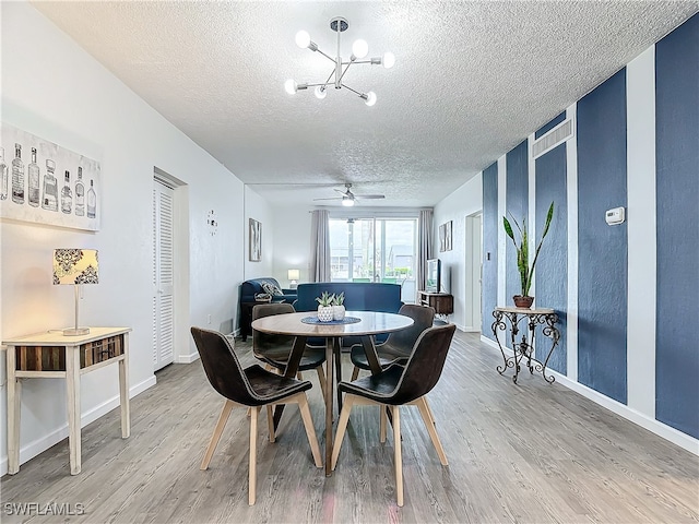 dining room with a textured ceiling, wood-type flooring, and ceiling fan with notable chandelier