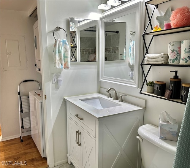 bathroom with stacked washer and dryer, vanity, wood-type flooring, and toilet