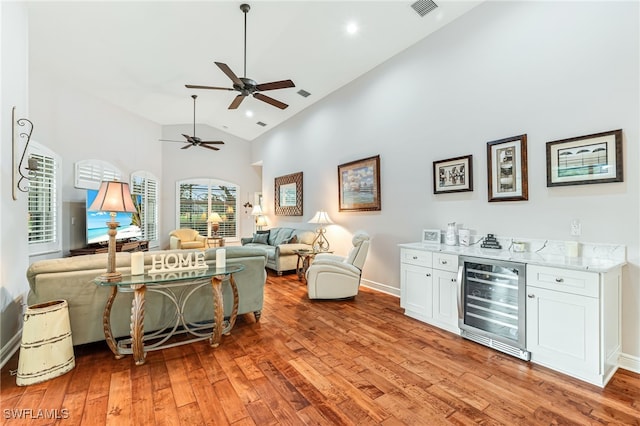 living room with ceiling fan, high vaulted ceiling, light hardwood / wood-style flooring, bar area, and wine cooler