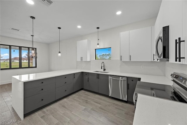 kitchen featuring appliances with stainless steel finishes, sink, pendant lighting, light hardwood / wood-style flooring, and white cabinetry