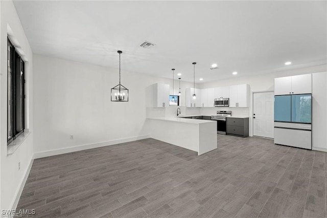 kitchen with appliances with stainless steel finishes, sink, wood-type flooring, white cabinetry, and hanging light fixtures