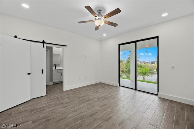 empty room featuring a barn door, ceiling fan, and light hardwood / wood-style floors