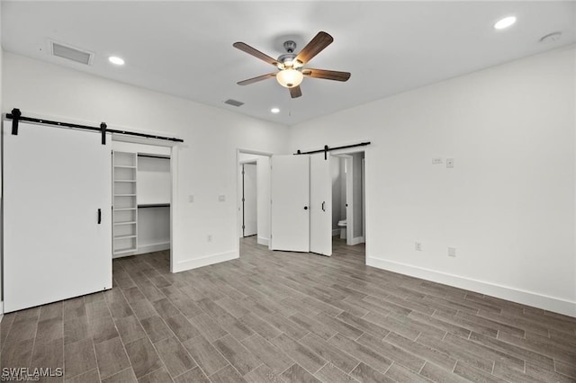 unfurnished bedroom with light wood-type flooring, ceiling fan, a barn door, a spacious closet, and a closet