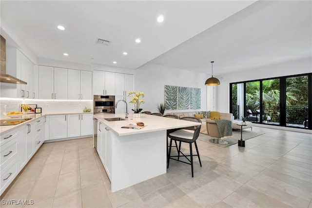 kitchen featuring sink, light tile patterned floors, an island with sink, pendant lighting, and white cabinets