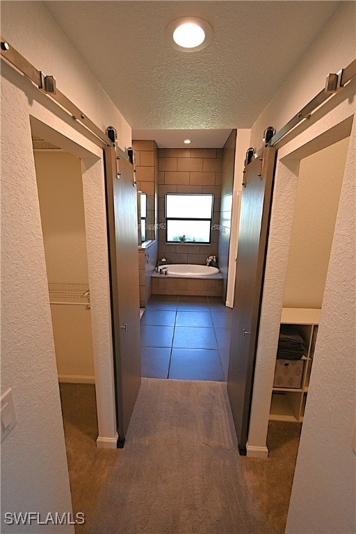 hallway featuring a barn door, a textured ceiling, and dark colored carpet