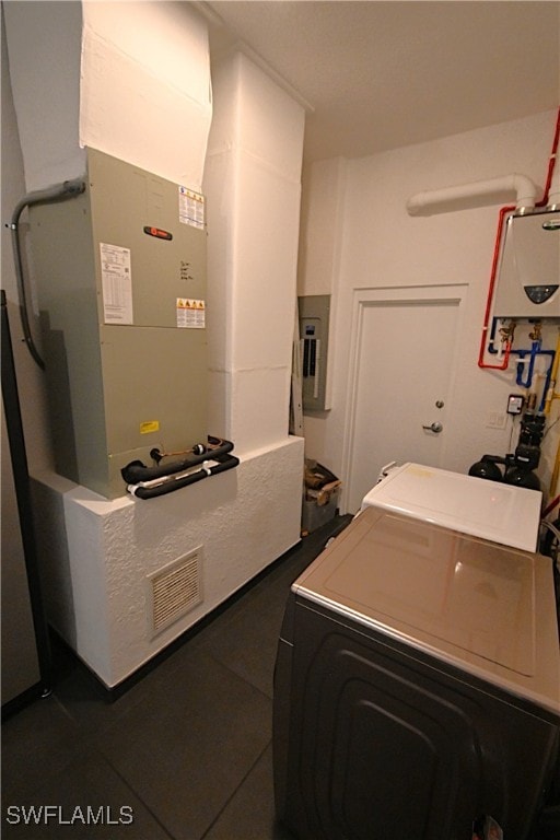 washroom featuring dark tile patterned flooring, tankless water heater, washer / dryer, and electric panel