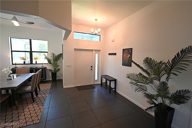 entrance foyer with ceiling fan with notable chandelier, dark tile patterned floors, and a textured ceiling